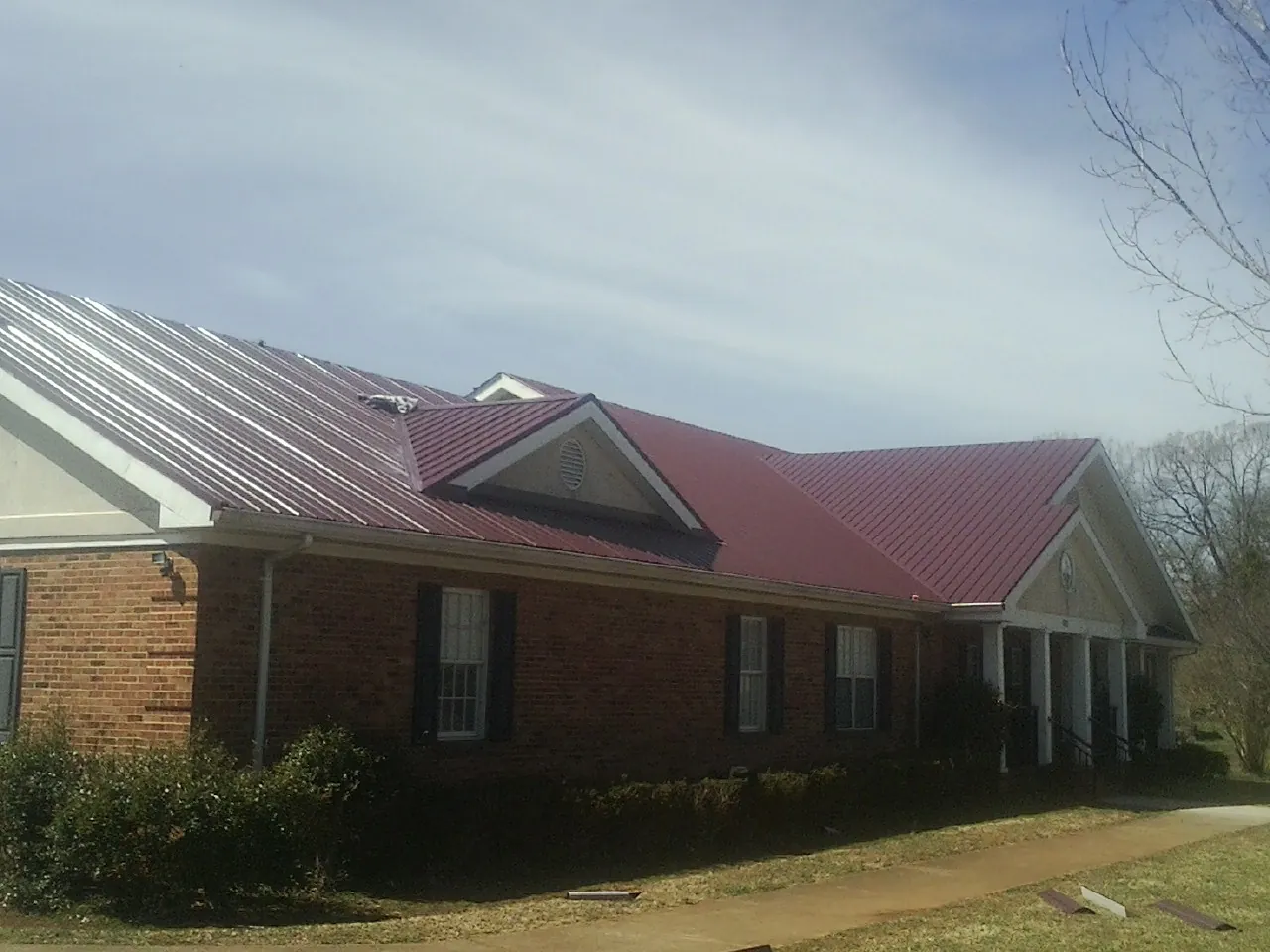 Red metal roof with gabled entries on a long brick building, from a Hail Damage Roof Repair job in Fremont
